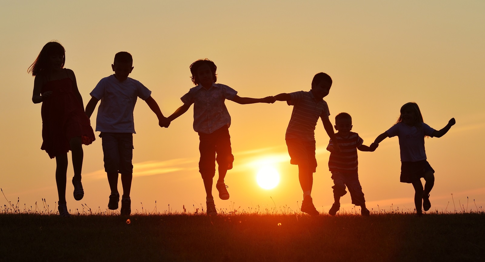 Happy children silhouettes on summer meadow running and jumping